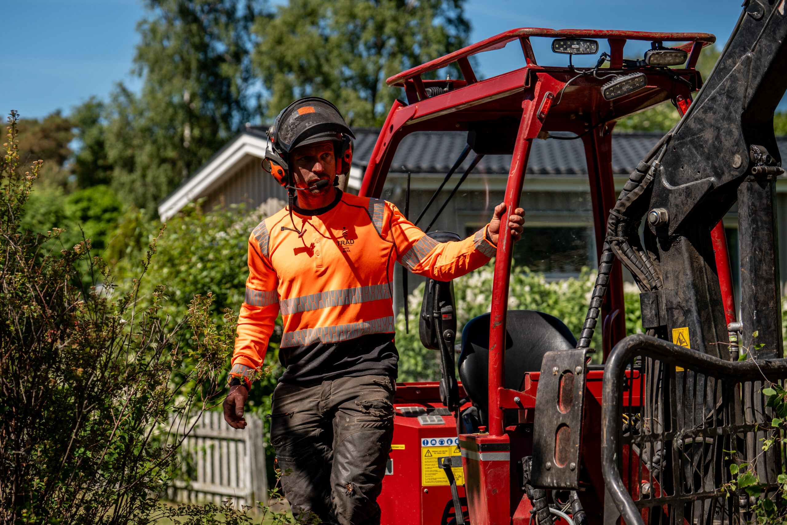 Arborist bredvid en röd bandgående maskin vid ett hus