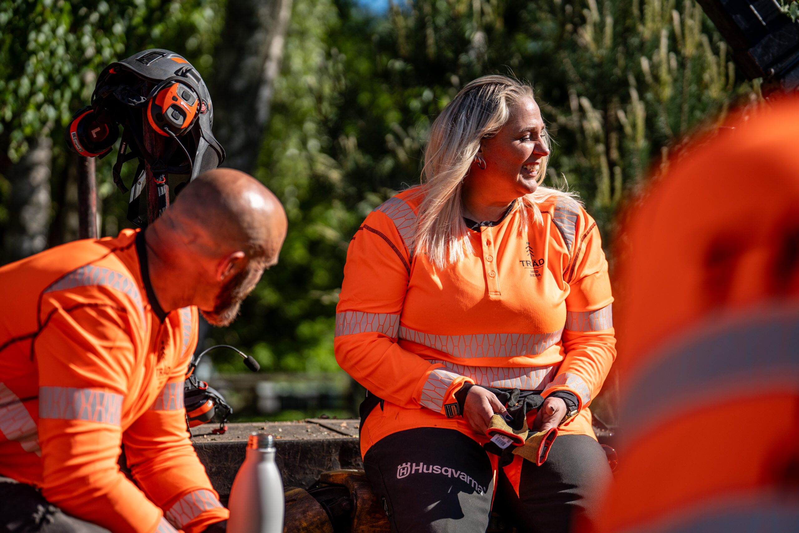 Två kollegor i orange arbetskläder pratar och skrattar i en paus